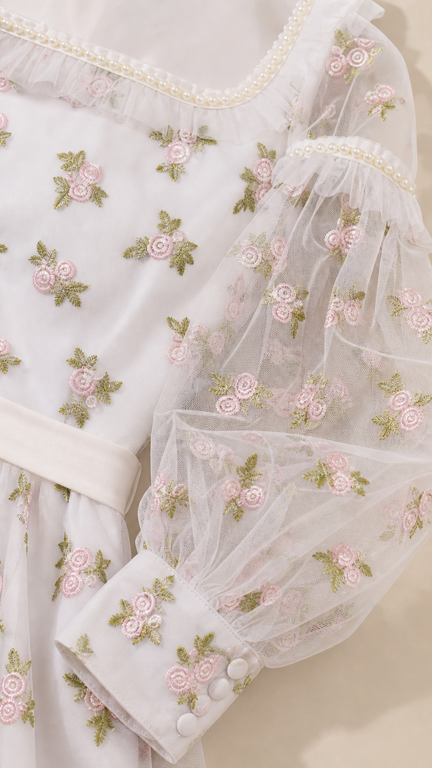 Close-up detail of floral embroidery, faux-pearl neckline, and sheer cuff sleeves
