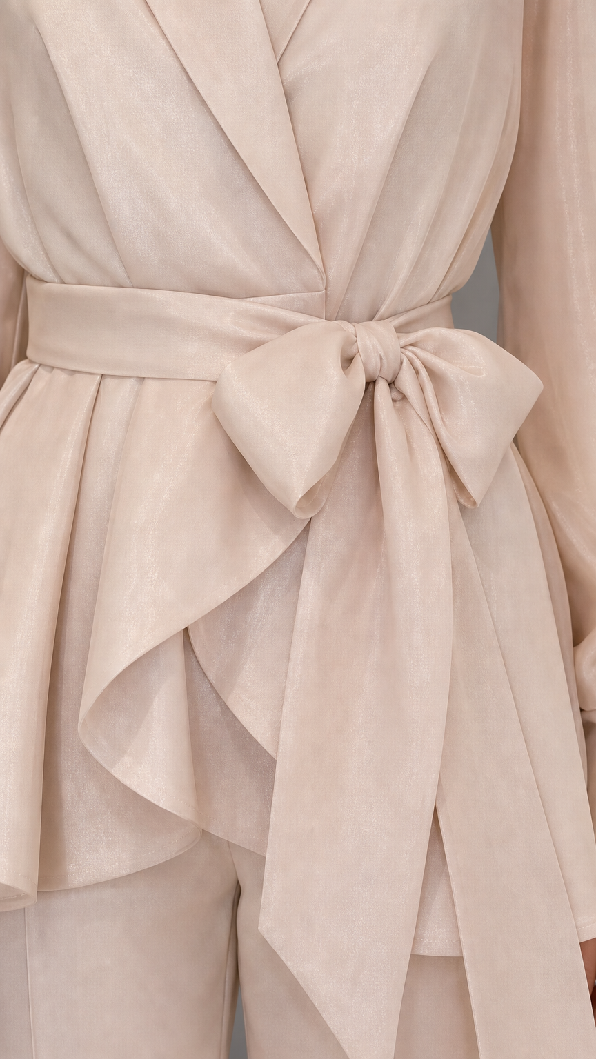 Close-up detail of self-tie bow and wrap peplum hem in beige