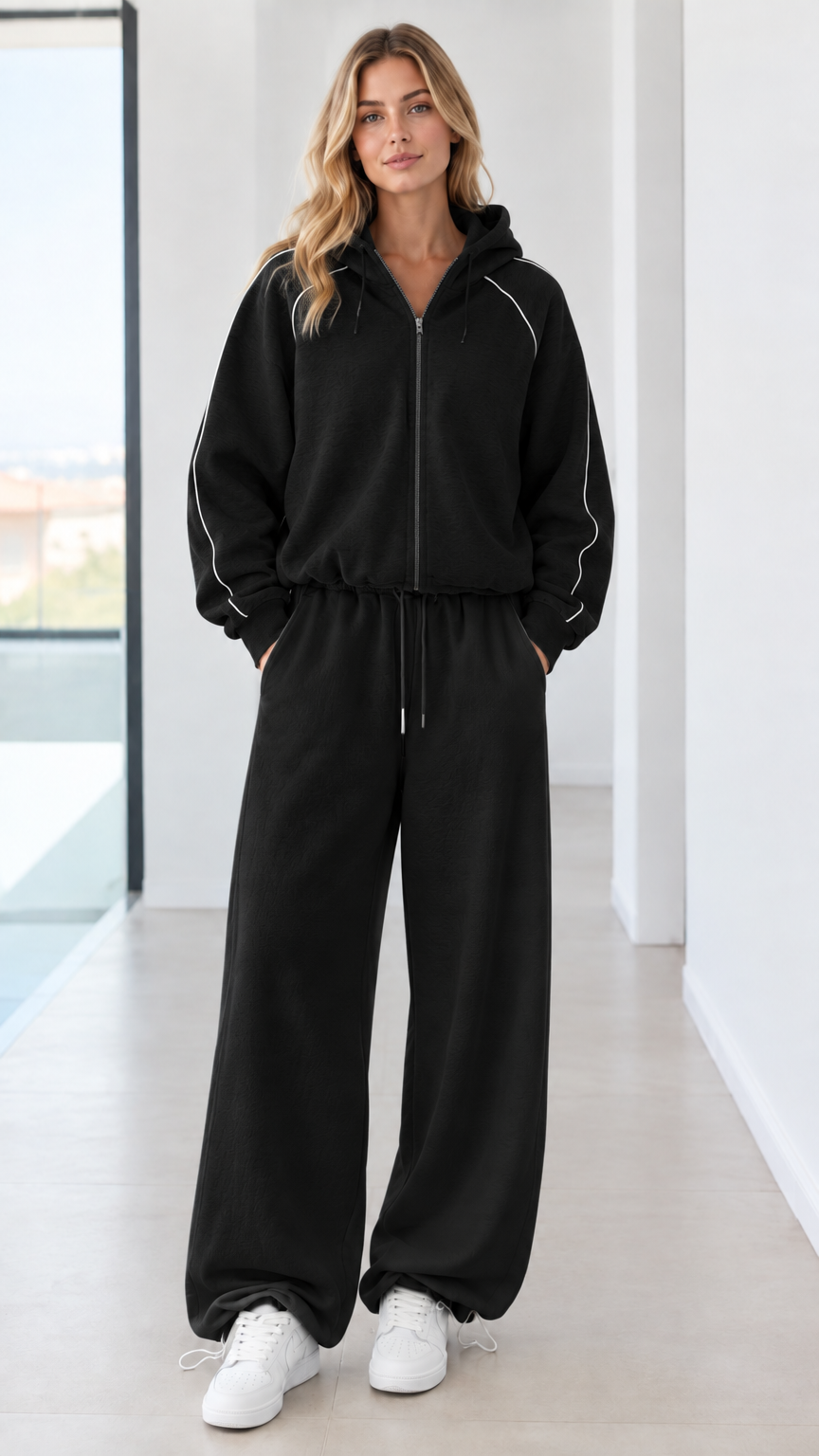 Full body studio shot of model wearing black zip-up hoodie and matching wide-leg sweatpants