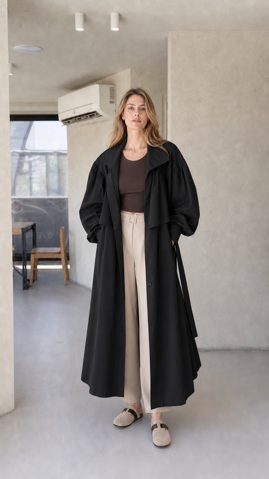 Model wearing black oversized maxi trench coat paired with cream wide-leg trousers