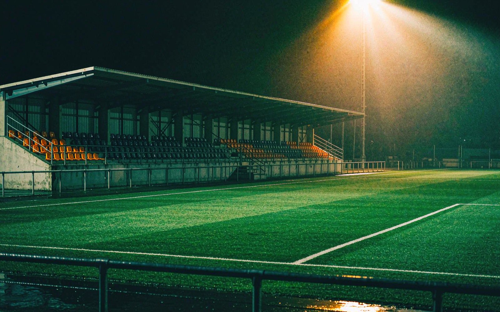 Empty technical area beside a floodlit pitch at night