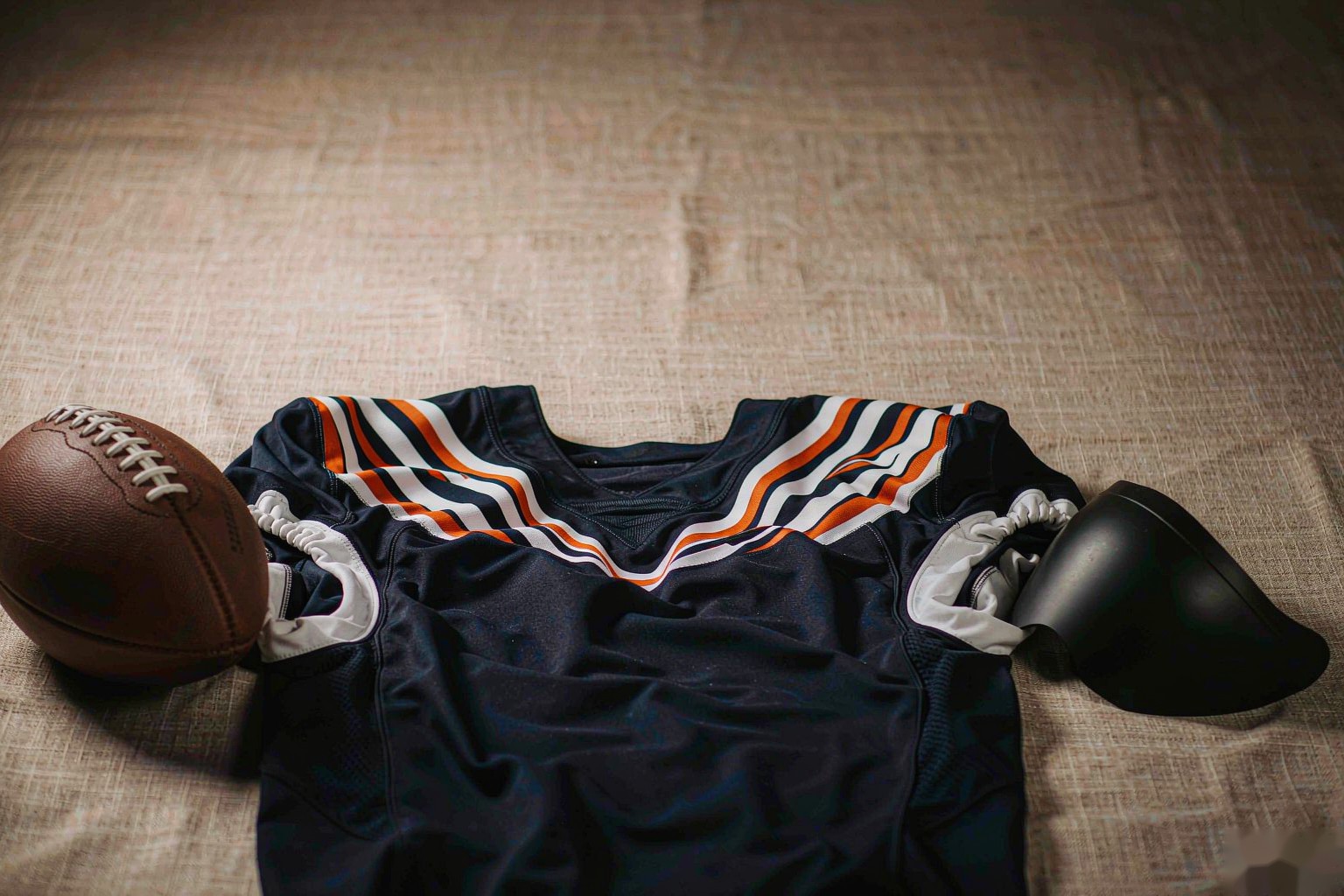 A navy american football jersey with a leather football and helmet visor on linen