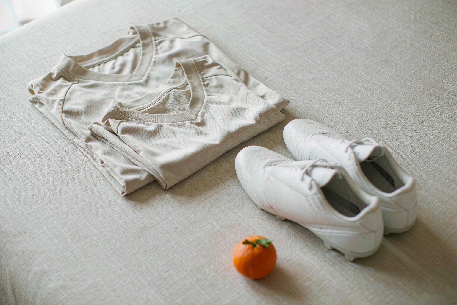 An adult and a kids soccer jersey folded together beside white boots