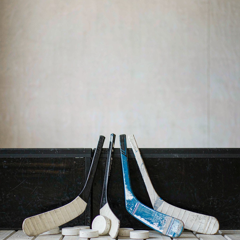 Hockey sticks and pucks lined up against a boards in an arena