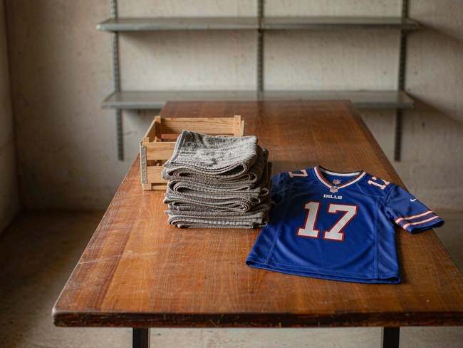 A royal blue Buffalo Bills football jersey laid flat on a wooden table in an equipment room beside a stack of folded grey towels