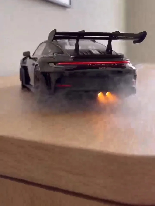 Rear of a black coupé with a wide spoiler, red light bar and mist over a wooden surface