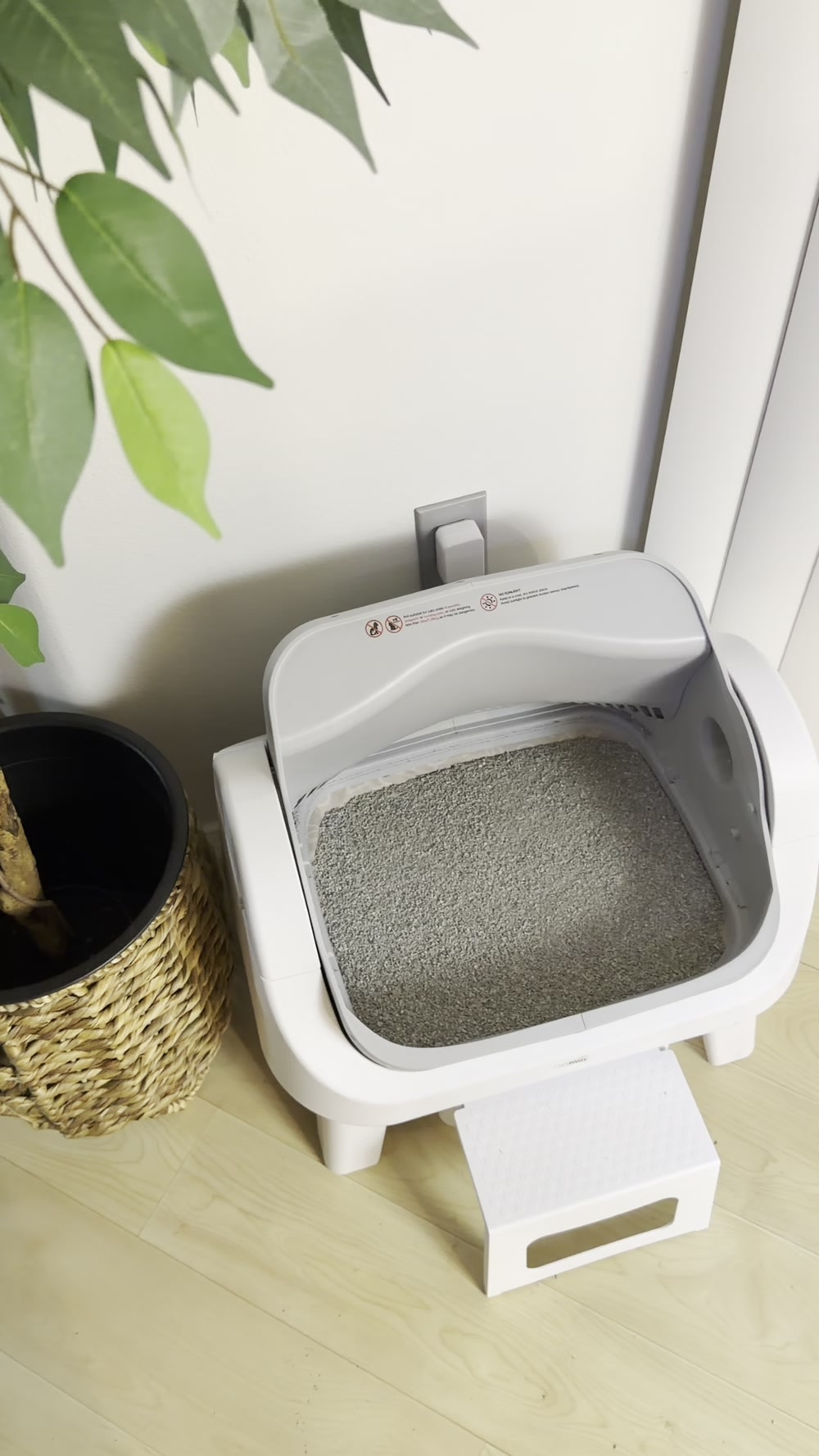 White and gray open-top automatic litter box with a front step in a home setting