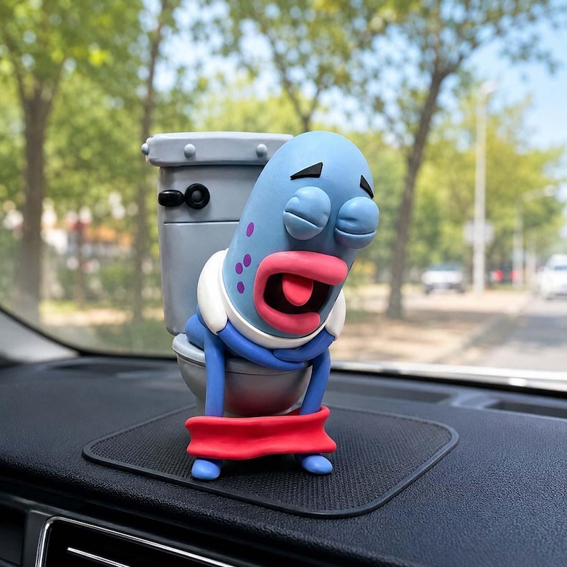 May include: A blue cartoon-style character with purple spots and pink lips sitting on a gray toilet. The character has closed eyes and an open mouth with a tongue sticking out. A bright red band wraps around the base of the toilet and the character.