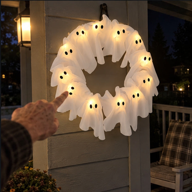 Older hand pointing at a glowing ghost on the wreath during a night porch display