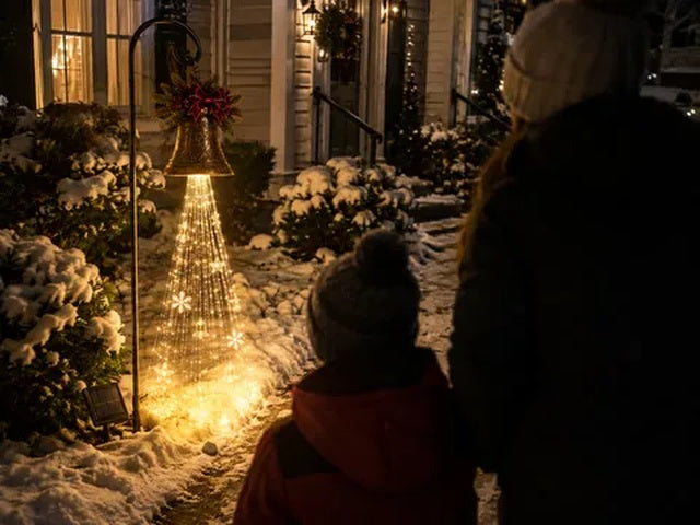 A family admiring the glowing Christmas bell yard light at night
