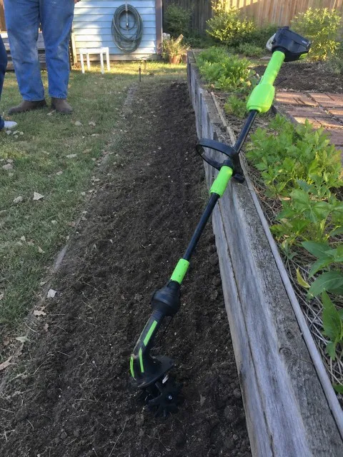 Cordless tiller resting beside a freshly worked narrow garden row
