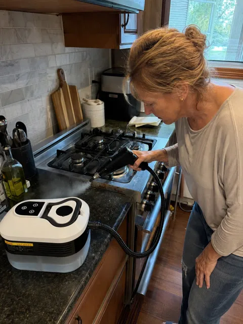 Customer using the white steam cleaner near a kitchen stovetop