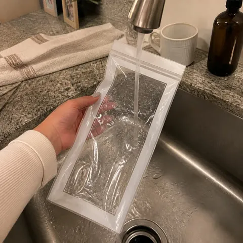 A long clear produce bag being rinsed in a home kitchen sink