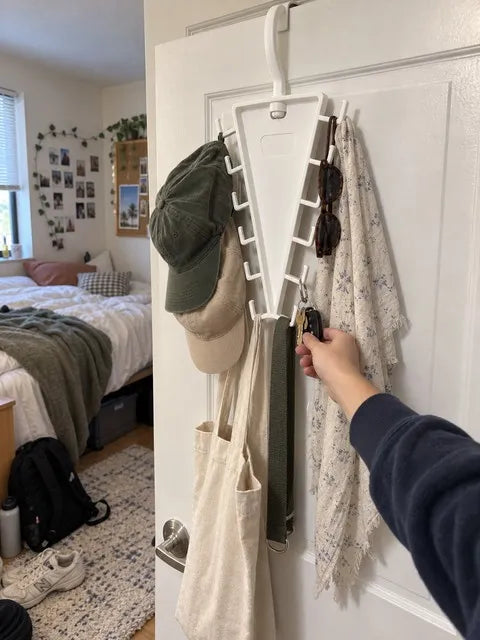 White V-shaped organizer holding hats, keys, sunglasses and a tote behind a bedroom door