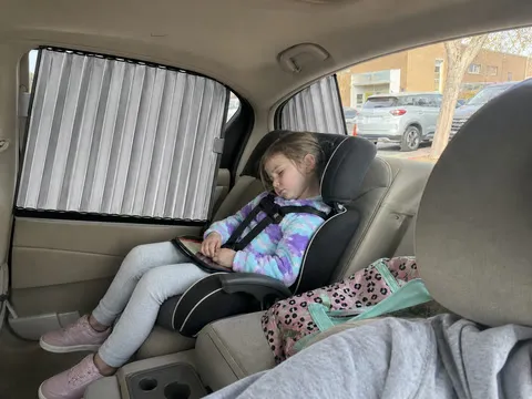 Child resting in the shaded rear seat during school pickup