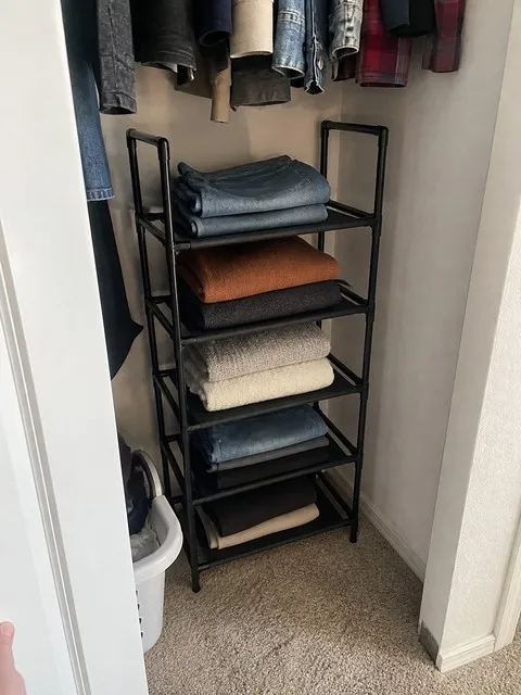 Five-tier rack holding folded jeans and sweaters in a small closet
