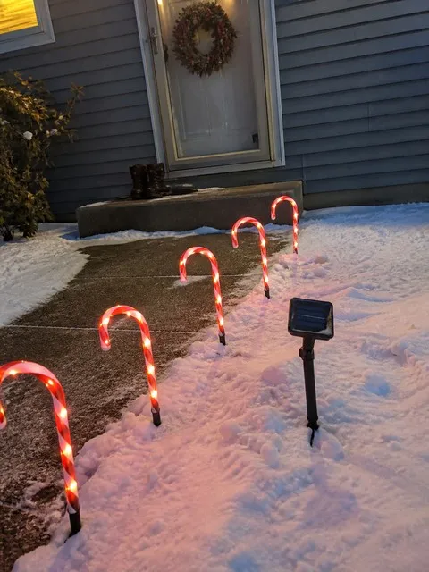 Five glowing candy cane lights along a snowy front walkway