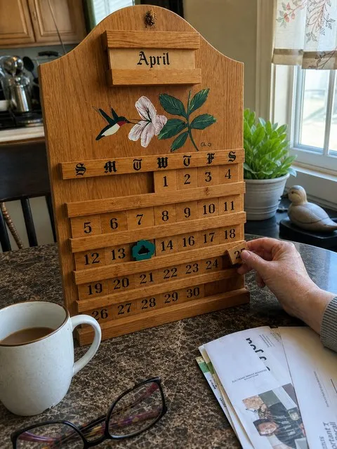 A wooden perpetual calendar beside coffee and morning mail