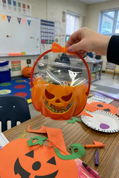 Teacher holding an orange pumpkin treat bag during a classroom Halloween party