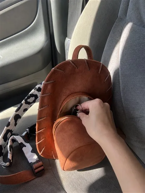 Hand opening a brown cowboy hat backpack on a car passenger seat