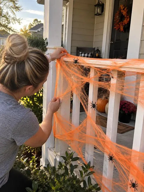 Orange spider web being stretched around a front porch railing