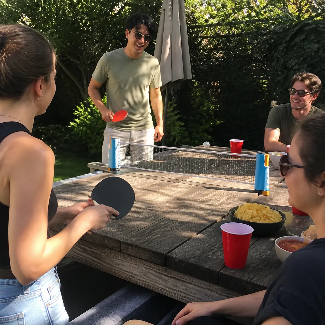 Friends playing table tennis on a backyard picnic table