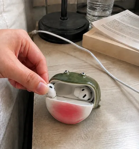 Green frog earbud case open on a bedside table