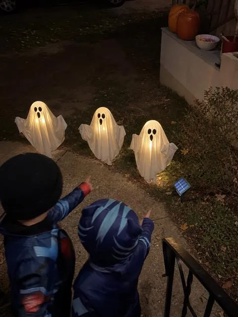Two children pointing at three glowing ghost lights on Halloween night