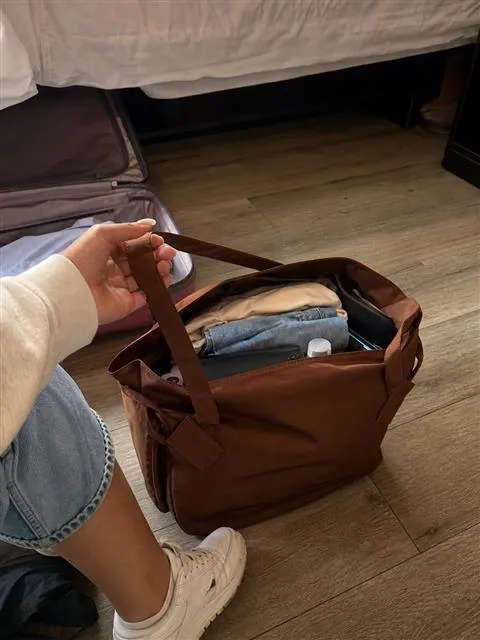 Brown tote filled with clothes beside a hotel bed