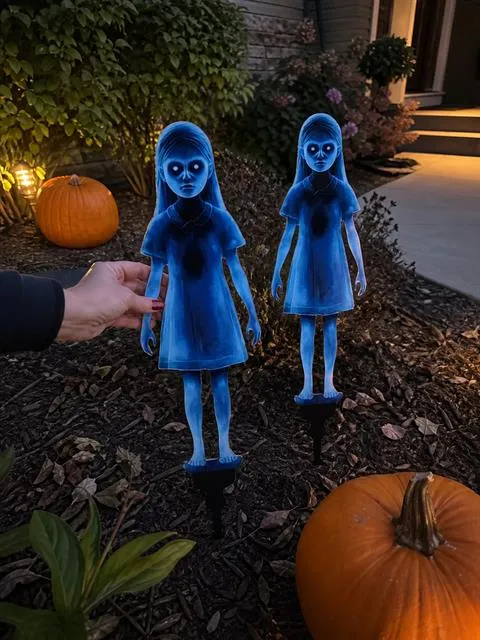 Two blue ghost-girl garden stakes being placed beside a pumpkin walkway