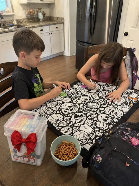 Siblings coloring the blanket at a kitchen table