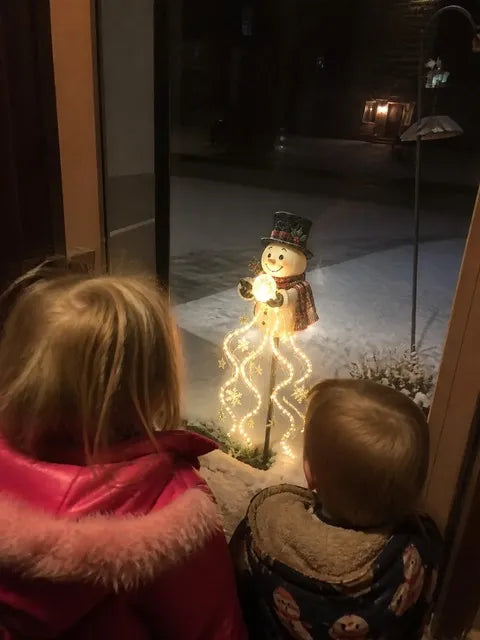 Children watching the illuminated snowman fountain light through a doorway at night