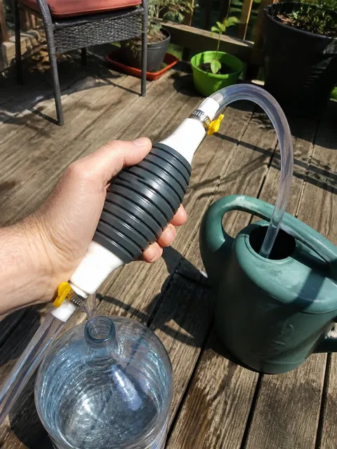 Hand using the siphon pump on a backyard deck