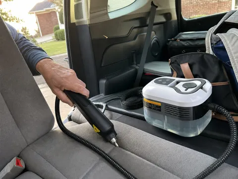 Customer using the white steam cleaner on car seat seams