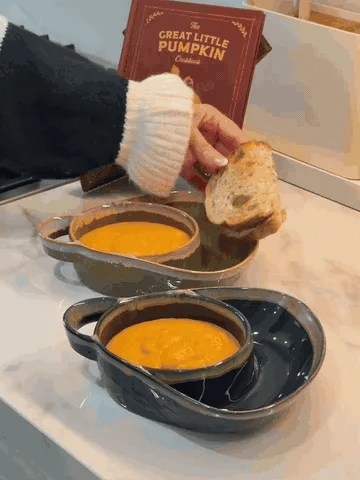 Soup being served into a divided ceramic bowl beside bread