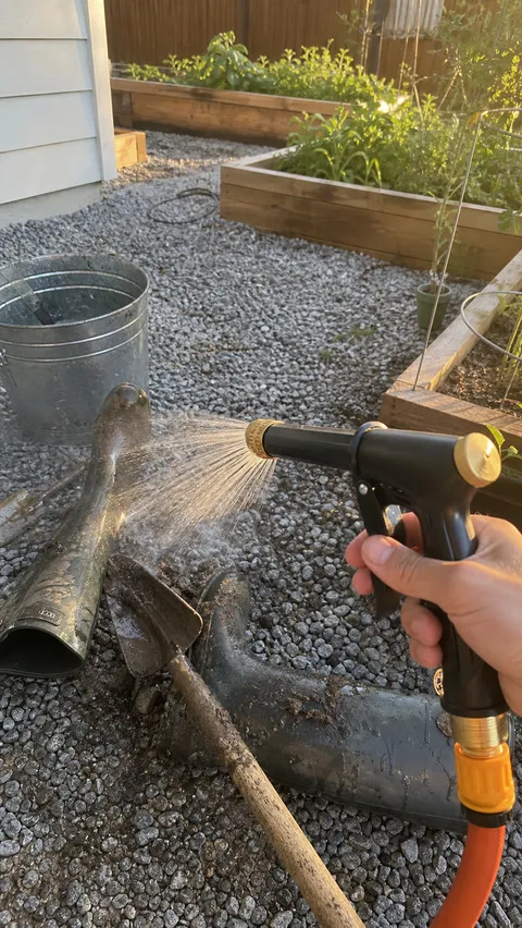 Muddy garden tools being cleaned with a wide spray outdoors