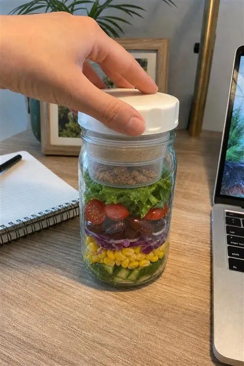 Closed layered salad jar beside a laptop at lunchtime