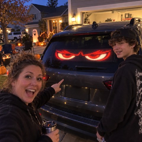 Family enjoying animated LED eyes on an SUV during a Halloween driveway gathering