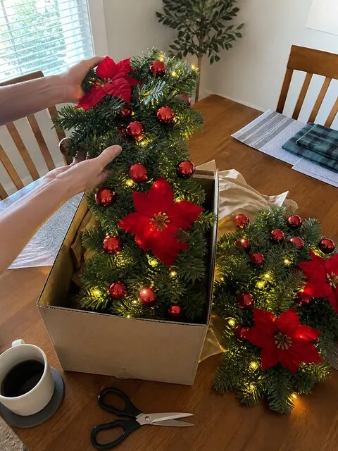 Hands lifting a decorated garland from a plain box on a dining table