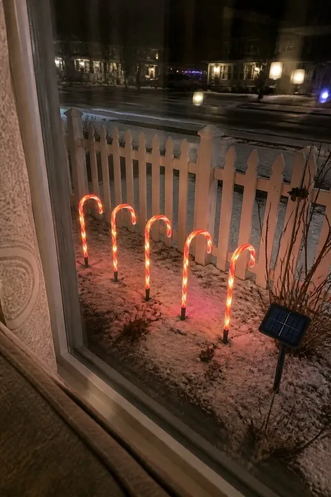Five glowing candy cane lights viewed through a living-room window