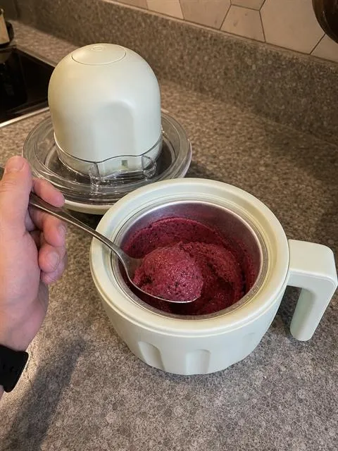 Berry sorbet being scooped from the open stainless-steel bowl after the top assembly is removed