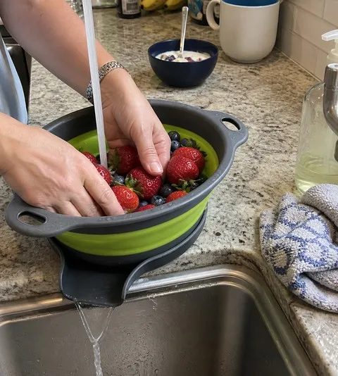 Hands rinsing berries in the large green colander beside a kitchen sink