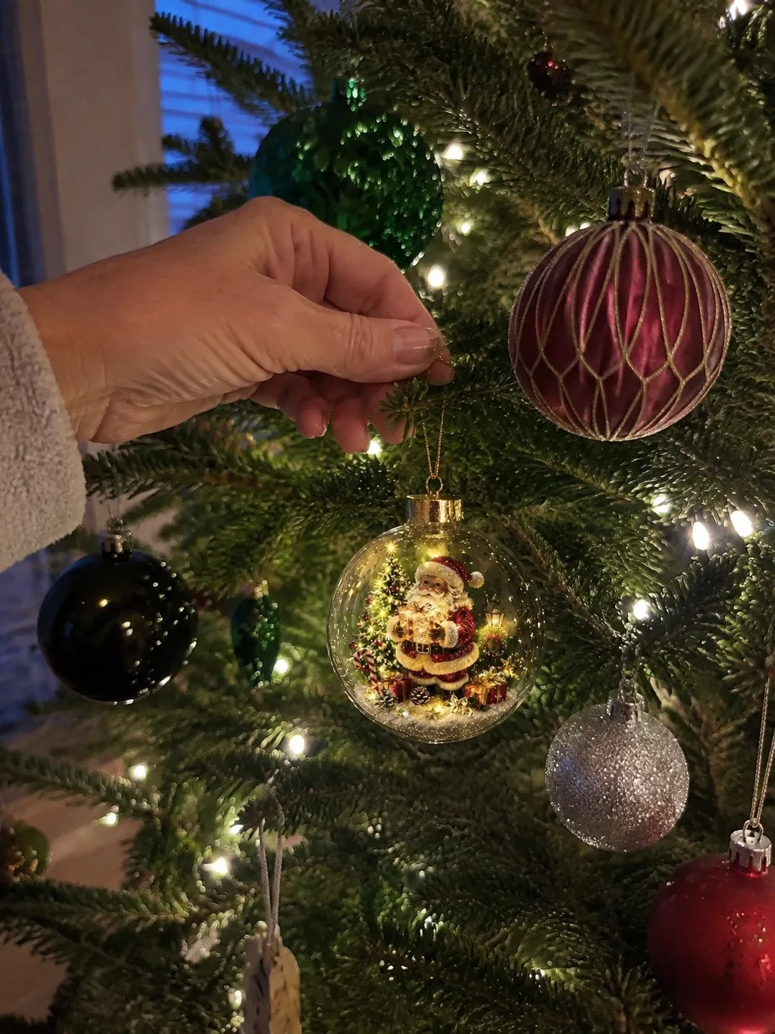 Santa ornament being hung on a family Christmas tree