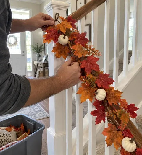 Hands attaching a white pumpkin maple garland to a stair rail