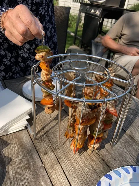 Cook lifting a finished skewer at a backyard gathering