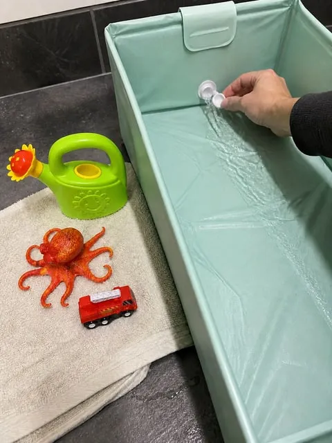 Hand opening the drain plug while the three bath toys dry nearby