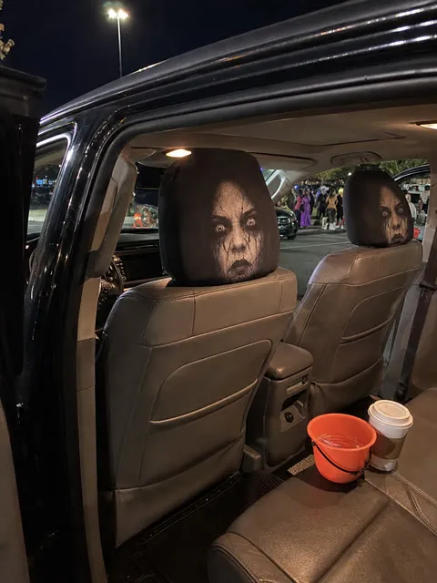 Casual nighttime trunk-or-treat photo with two scary headrest covers
