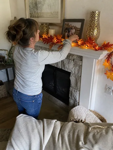 Maple leaf light garland being arranged on a family-room mantel