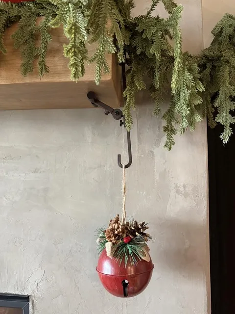 Black mantel hanger holding a holiday bell below greenery