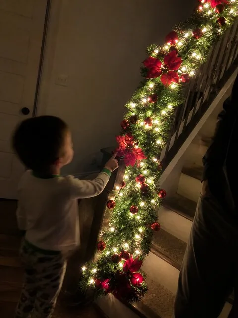 Child admiring a glowing garland on a staircase at night